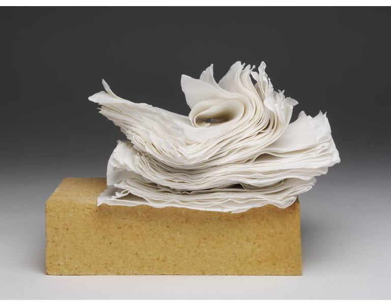 What resembles a yellow stone brick lying lengthwise with what resembles curls of white paper on top of it. A contemporary Dehua porcelain artwork