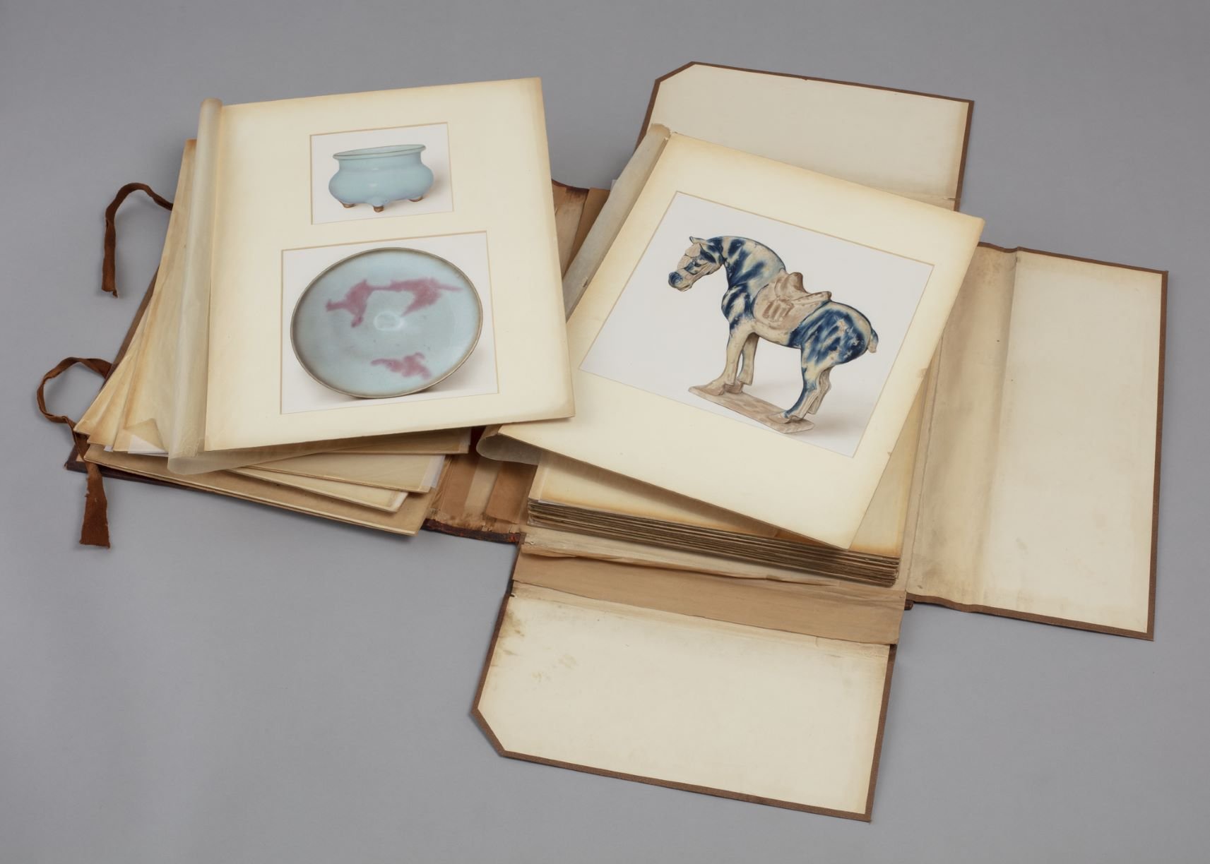 A folder of colour illustrations of Chinese ceramics showing a Junyao tripod and purple-splashed bowl on the left and a Tang blue splashed sancai horse on the right