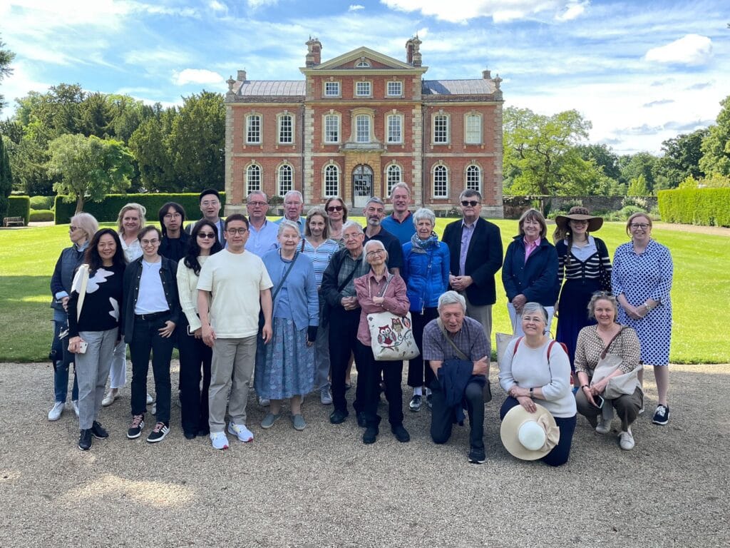 An OCS Tour group of 25 in front of a large house smiling at the camera