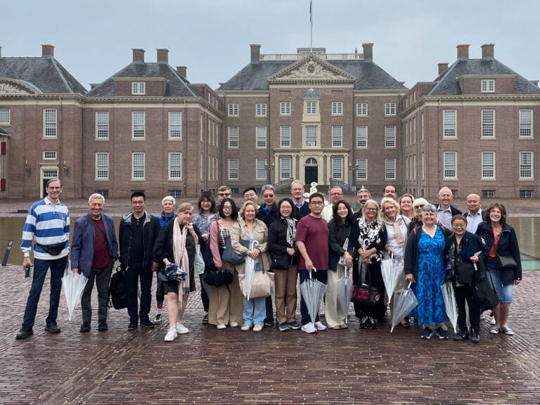 An OCS tour group of 27 people standing in front of a building smiling at the camera