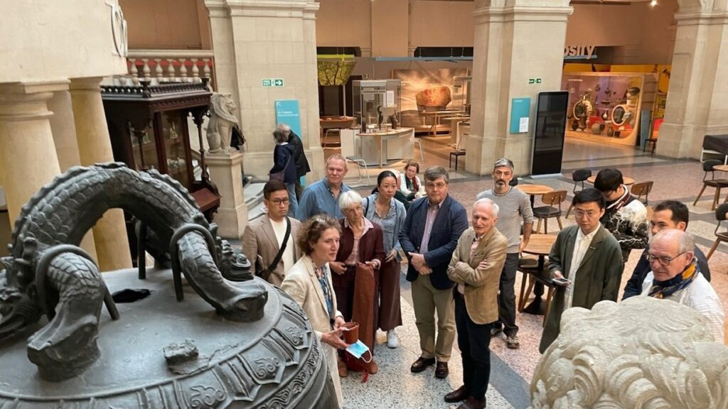 OCS visit showing a group of 14 attendees in a museum in front of a large bronze bell
