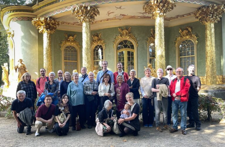 OCS Tour group of 24 people in front of a green and gold palace smiling at the camera